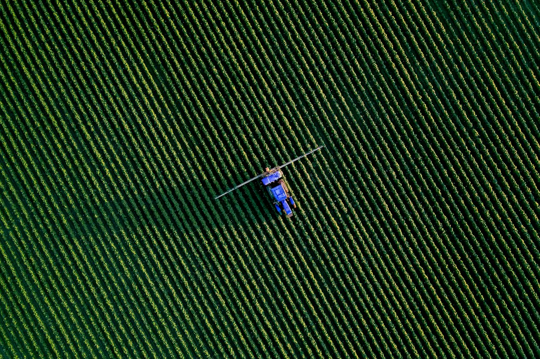 Aerial view of a blue tractor spraying a large green field (illustrative image)